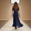 Woman in a navy blue off-shoulder dress walking on a runway.