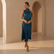 Woman in a teal dress standing in an archway with a neutral background