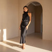 Woman wearing a black satin dress standing in a sunlit room with an archway.