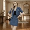 Woman in a blue textured outfit standing in an elegant room with wooden floors and decorative walls.