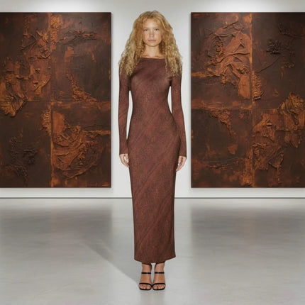 Woman in a long brown dress standing between two large textured paintings.