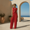 Woman in a red jumpsuit standing in a sunlit outdoor setting with arches and blue sky.