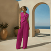 Woman in a pink outfit standing in a sunlit outdoor setting with arches and blue sky.