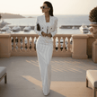 Woman in a white pinstripe suit standing on a balcony with a waterfront view.
