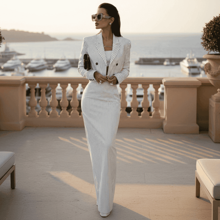 Woman in a white pinstripe suit standing on a balcony with a waterfront view.