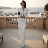 Woman in a white pinstripe suit standing on a balcony with a waterfront view.
