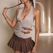 Woman wearing a light gray halter top with brown straps and a pleated brown skirt, standing against a neutral background.