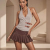 Woman wearing a light gray sleeveless top with a brown pleated skirt in an indoor setting.