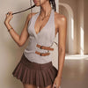 Woman wearing a light gray halter top with brown straps and a pleated brown skirt, standing against a neutral background.