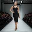 Model wearing a black NORVANE Riviera Bandage Dress on a fashion show runway with an audience.