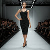 Model wearing a black NORVANE Riviera Bandage Dress on a fashion show runway with an audience.