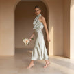Woman in a light green dress holding flowers in a sunlit room with arches.