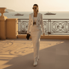 Woman in a white pinstripe suit walking on a balcony with a scenic ocean view.