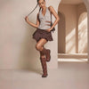 Woman in a stylish outfit with a skirt and knee-high boots in a softly lit room.
