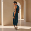 Woman in a teal dress standing in a sunlit architectural setting