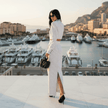 Woman in a white dress standing in front of a marina with yachts and buildings.