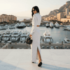 Woman in a white dress standing in front of a marina with yachts and buildings.