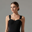 Woman wearing a black NORVANE Riviera Bandage Dress with gold accents against a gray background