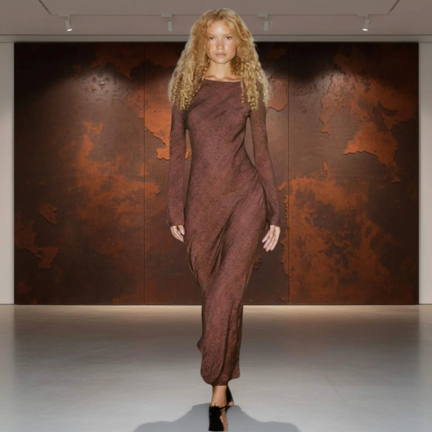 Woman in a brown dress standing against a textured brown wall.