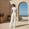 Woman in a white outfit standing on a sunlit terrace with arches and a view of the sea.