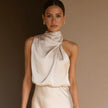 Woman wearing a beige halter neck dress against a brown background