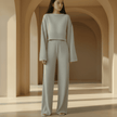 Woman wearing a light gray outfit standing in an architectural setting with arches.