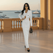 Woman in a white pinstripe suit standing on a balcony with a waterfront view.