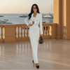 Woman in a white pinstripe suit standing on a balcony with a waterfront view.