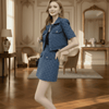 Woman in a blue outfit standing in an elegant room with wooden floors and decorative walls.