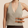 Woman wearing a beige halter top with brown leather straps on a beige background