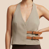 Woman wearing a beige halter top with brown leather straps on a beige background