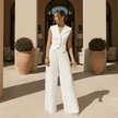 Woman in a white outfit standing on a sunlit terrace.