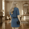 Woman in a blue dress standing in an elegant room with wooden floors and decorative walls.