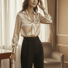 Woman wearing a beige blouse and black pants in a room with curtains and a chair.