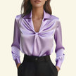 Purple satin blouse with a knot detail worn by a model on a beige background