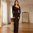 Woman in a black one-shoulder dress standing in an elegant room with wooden floor and large mirror.