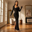 Woman in a black evening gown standing in an elegant room with large windows and decorative elements.