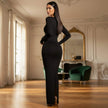 Woman in a black evening gown standing in an elegant room with a large mirror and green chair.